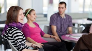 Three young people sitting in a classroom environment talking.